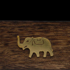 Zoom macro sur le motif éléphant doré, d'une boîte support d'encens en bois, sur fond noir.