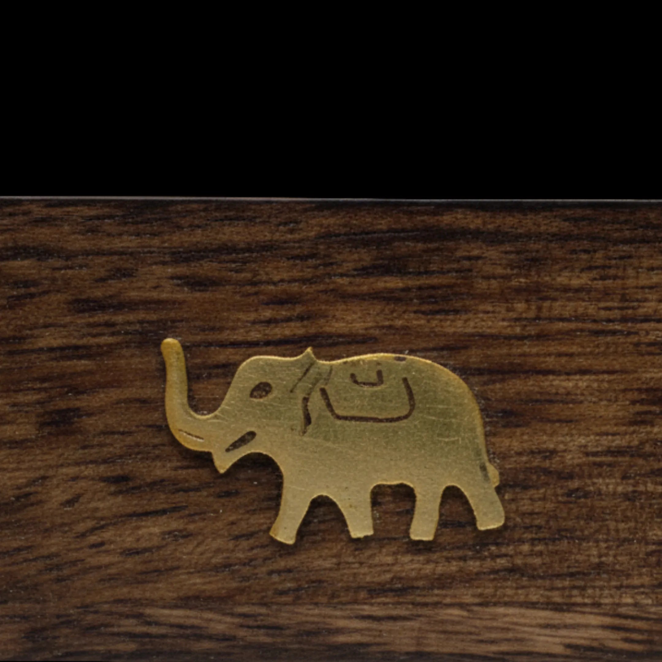 Zoom macro sur le motif éléphant doré, d'une boîte support d'encens en bois, sur fond noir.