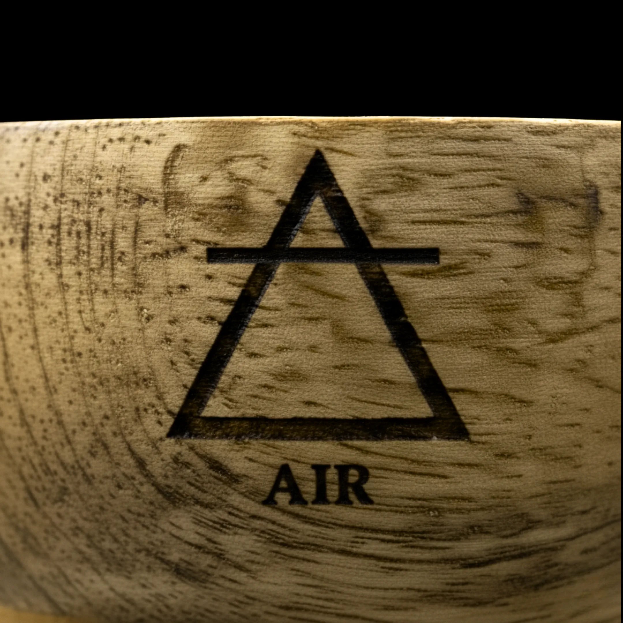 Bol en bois de manguier avec un zoom macro sur le symbole de l'élément air, gravé sur le haut du bol, sur fond noir.