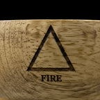 Bol en bois de manguier avec un zoom macro sur le symbole de l'élément feu, gravé sur le haut du bol, sur fond noir.