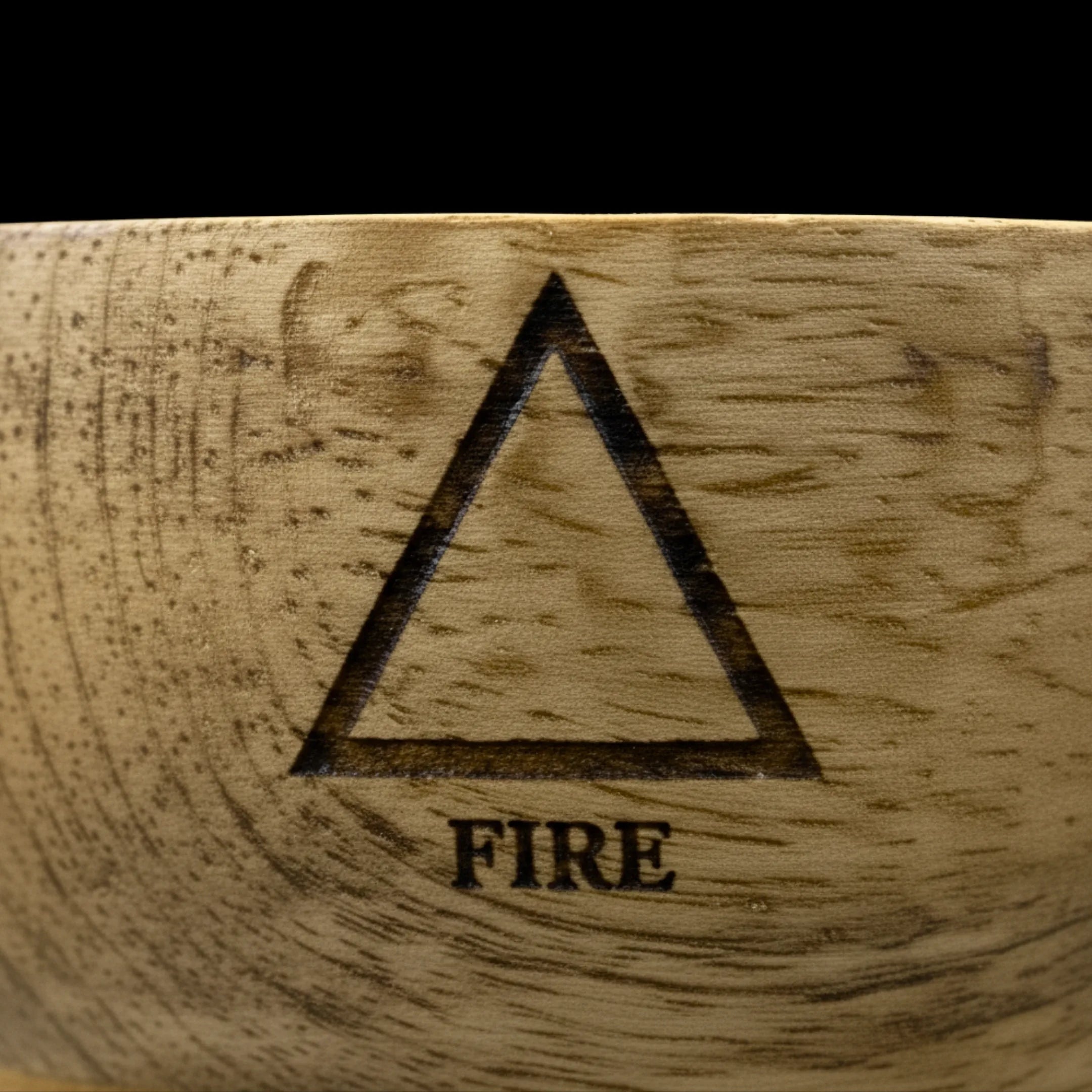 Bol en bois de manguier avec un zoom macro sur le symbole de l'élément feu, gravé sur le haut du bol, sur fond noir.