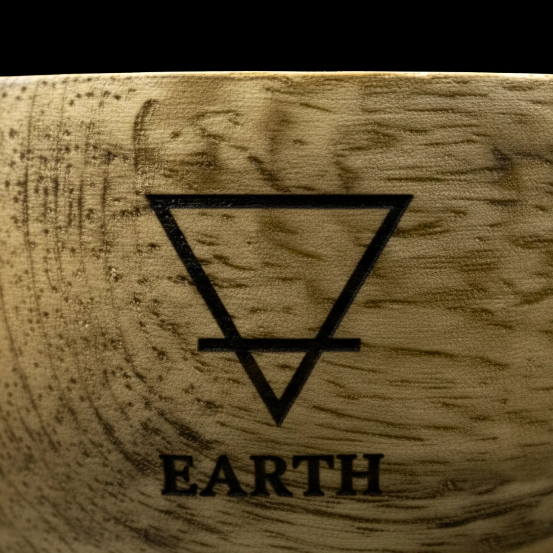 Bol en bois de manguier avec un zoom macro sur le symbole de l'élément terre, gravé sur le haut du bol, sur fond noir.