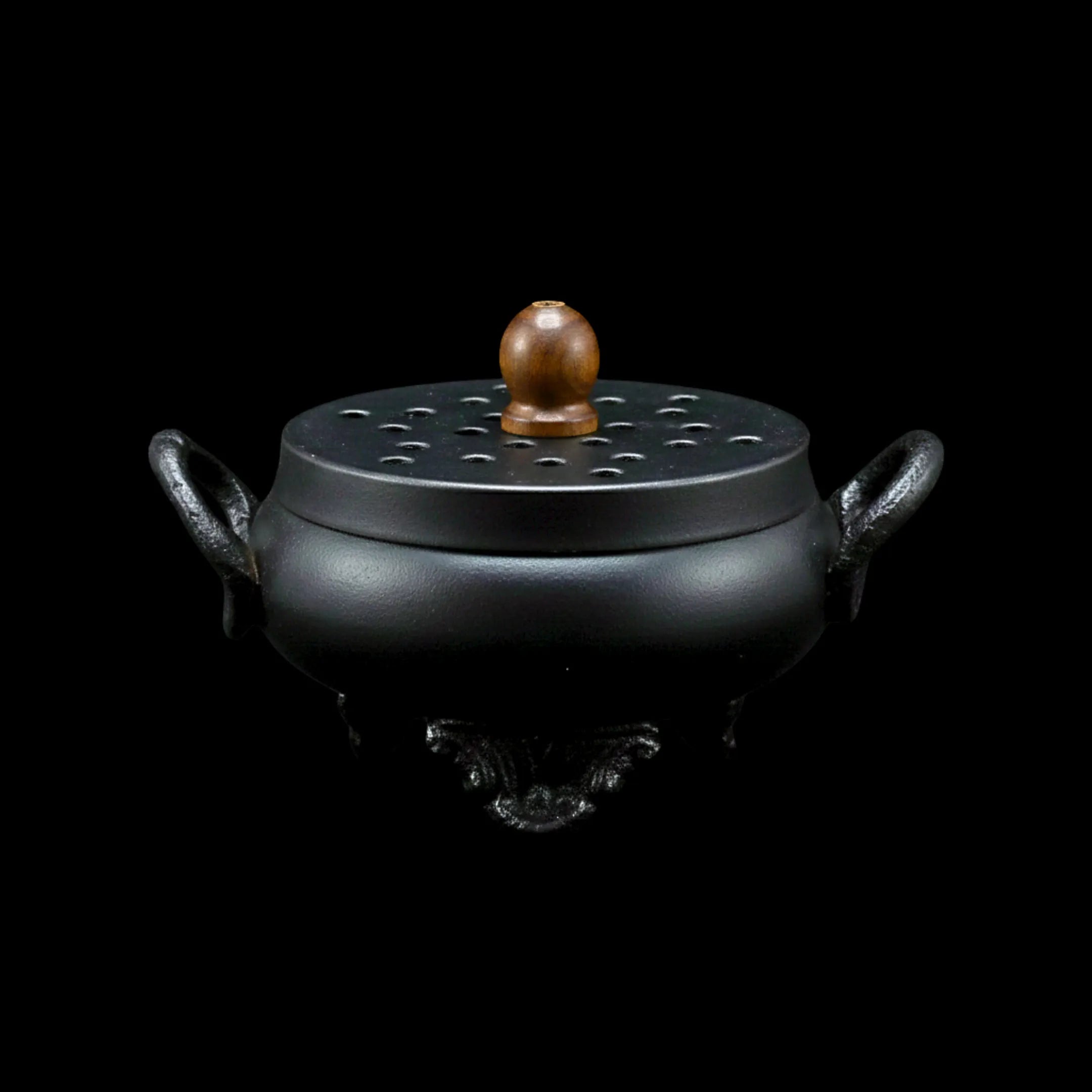Brûleur d'encens en fonte, en forme de chaudron, avec couvercle et poignée en bois, sur fond noir.
