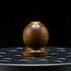 Vue macro sur la poignée en bois d'un couvercle de brûleur à encens en fonte, sur fond noir.