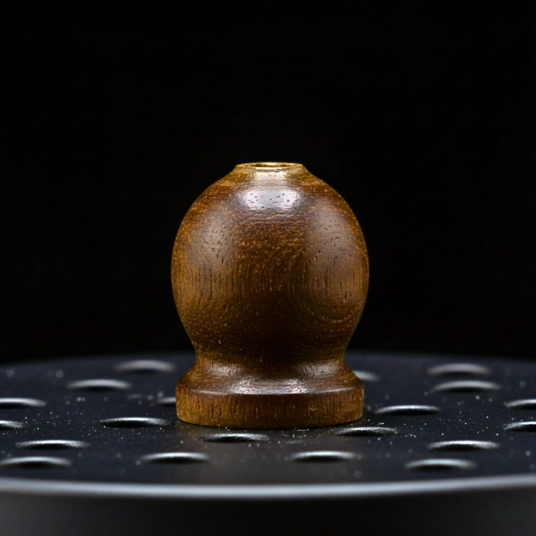 Vue macro sur la poignée en bois d'un couvercle de brûleur à encens en fonte, sur fond noir.