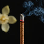 Vue macro de bâtonnets d'encens Nag Champa Satya en train de brûler, avec fleur de magnolia champaca, sur fond noir.